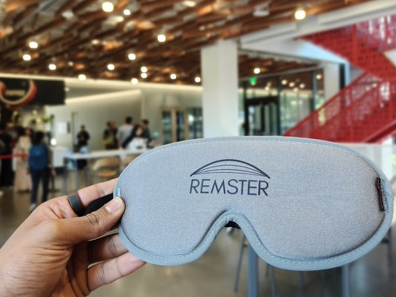 A hand holding the Remster sleep mask in a bright campus building